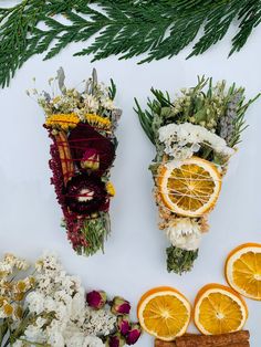 three dried oranges and flowers arranged on a white surface with pine branches, twigs, and other foliage