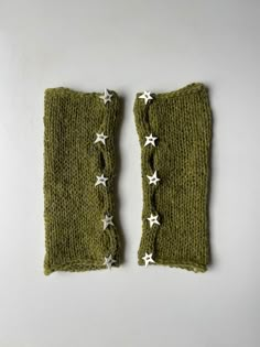 two green knitted mittens with white stars on the top and bottom, sitting side by side