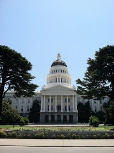 a large white building with a dome and trees in the foreground on a sunny day