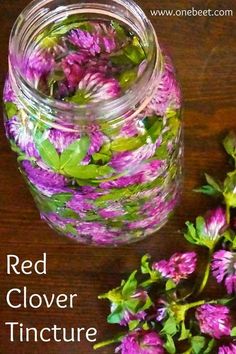 purple and green flowers in a glass jar on a wooden table next to some leaves