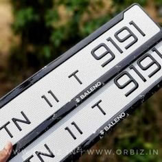 two white and black street signs in the palm of someone's hand with trees in the background