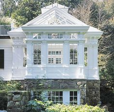 a white house sitting in the middle of a lush green forest next to a stone wall