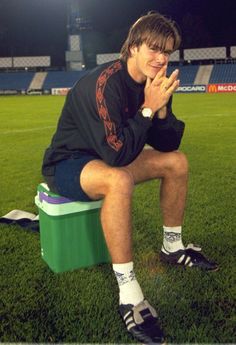 a man sitting on top of a green box in the middle of a soccer field