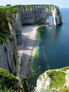 the beach is next to an arch in the cliff