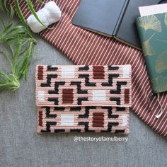 a cross - stitch purse sitting on top of a table next to a notebook and flowers