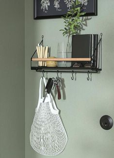 a wall mounted shelf with two hooks and a wire bag hanging from it's side