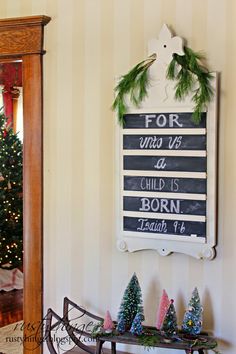 a sign that says for christmas hangs on the wall next to a table with small trees