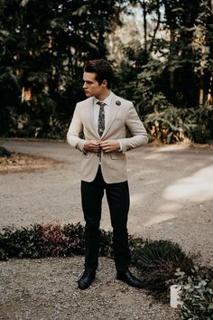 a man wearing a suit and tie standing in the middle of a road with trees behind him