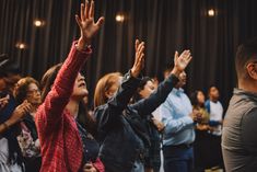 a group of people standing in front of a stage with their hands up to the sky