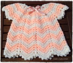 a pink and white crocheted baby sweater with a bow on the front, sitting on a wooden surface