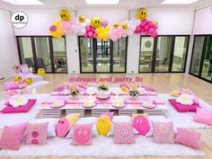 a table set up for a party with pink and yellow decorations on the tables, balloons in the air