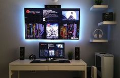 a desk with a monitor and speakers on it in front of a wall mounted television