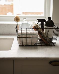 a kitchen counter with soap, dish towels and other items in a basket on it