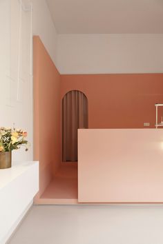 an empty room with pink walls and white flooring is seen in this image, there are flowers on the counter