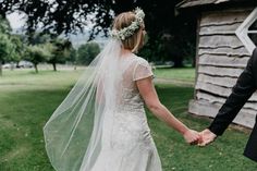 a bride and groom hold hands as they walk through the grass in front of a barn