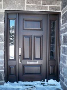 the front door to a home with snow on the ground and brick wall behind it