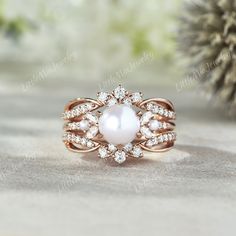 a white pearl and diamond ring sitting on top of a table next to a pine cone