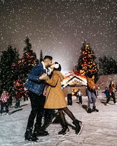 a man and woman kissing in front of a christmas tree on a snow covered field