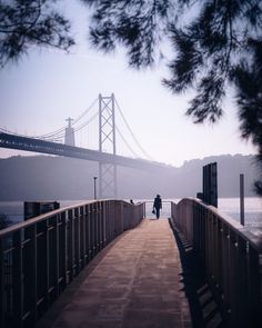 a person walking on a bridge over water with a large suspension bridge in the background