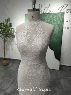 a white dress on display in front of a wall with a green plant behind it