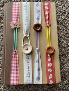 the book is lined up with different colored ribbons and buttons on them, along with two wooden spoons