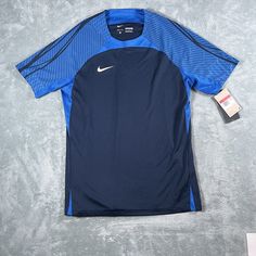 Introducing the Nike Men's Dri-Fit Strike Top, a stylish and functional addition to any athlete's wardrobe. This pullover T-shirt features a crew neck and short sleeves, with a slim fit that flatters the wearer's physique. The Nike logo is prominently displayed in blue on the shirt's front, adding a touch of personality to the garment. This top is machine washable and comes in size L. It is perfect for soccer and football and is suitable for wear in all seasons. The Nike Dri-FIT product line ensures that the garment is moisture-wicking, keeping the wearer cool and comfortable during physical activity. Blue Jersey T-shirt For Sportswear, Blue Jersey T-shirt Sportswear, Blue Short Sleeve Training T-shirt, Blue Technical Sports T-shirt, Technical Crew Neck Tops For Sports Events, Crew Neck Tops For Sports Events, Sports Crew Neck Jersey Shirt, Jersey Crew Neck Sports Shirt, Sports Jersey Shirt With Crew Neck