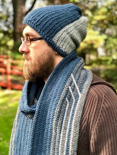 a man wearing a knitted hat and scarf in front of a wooden fence with trees