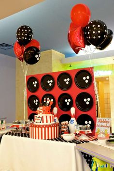 a table topped with lots of black and white balloons next to a red cake covered in polka dots