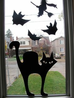 a window with some paper bats flying in the air and a cat sitting on top of it