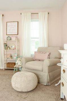 a baby's room with pink walls, white furniture and a large round ottoman