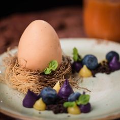 a white plate topped with an egg next to blueberries and other fruit on top of it