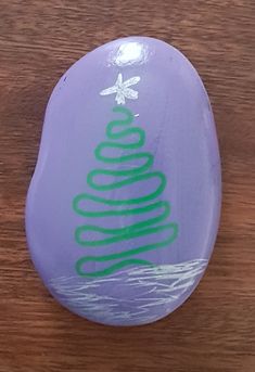 a purple rock with a green christmas tree on it sitting on top of a wooden table