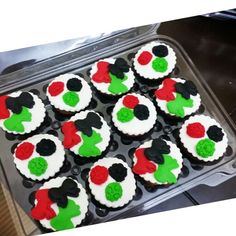 twelve decorated cupcakes in a plastic container on a stove top with black, white and red frosting