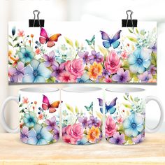 three coffee mugs with colorful flowers and butterflies on them, sitting on a table