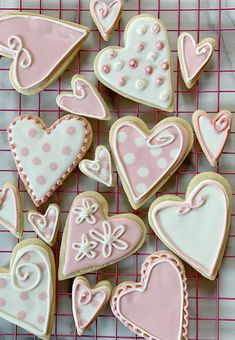 decorated cookies on a cooling rack with pink and white icing in the shape of hearts