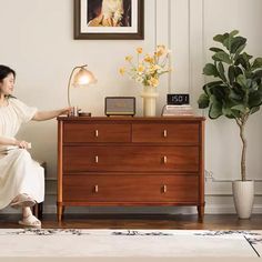 a woman sitting on a chair in front of a dresser with flowers and a clock