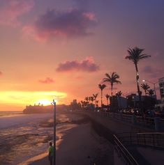 the sun is setting over the beach with palm trees in the foreground and buildings on the other side