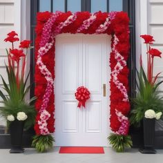 a white door with red and pink flowers next to potted plants in front of it