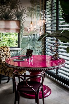 a pink table with two chairs and a laptop on it in front of a window