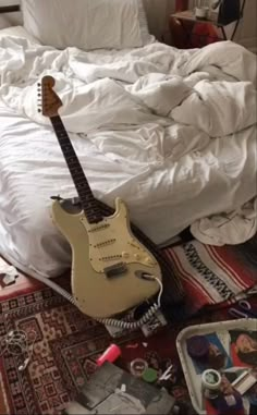 a guitar laying on top of a bed next to a white comforter and pillows