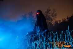 a scary scarecrow with glowing eyes and long hair sitting on a fence at night