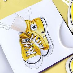 a drawing of a pair of yellow converse shoes on top of a paper with markers