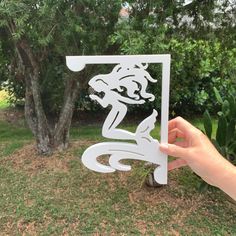 a person holding up a cut out of paper in front of a tree and grass area