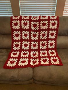 a red crocheted blanket sitting on top of a couch next to a window