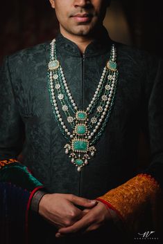 a man wearing a green and gold outfit with beads on his neck, standing in front of a dark background