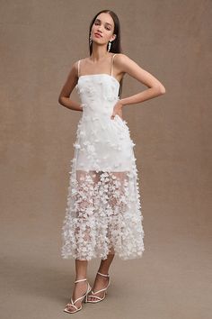 a woman is wearing a white dress with flowers on the skirt and heels, standing in front of a brown background