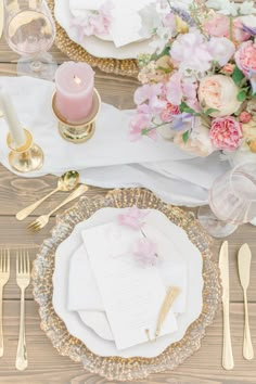 the table is set with white and gold plates, silverware, pink flowers and candles