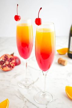 two wine glasses filled with orange and raspberry punch on a marble countertop