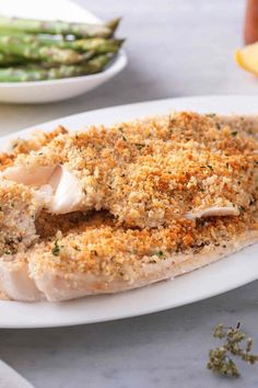 a white plate topped with fish covered in seasoning next to asparagus and lemon wedges