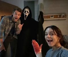 two people standing next to each other in front of a creepy man with a ghost mask on